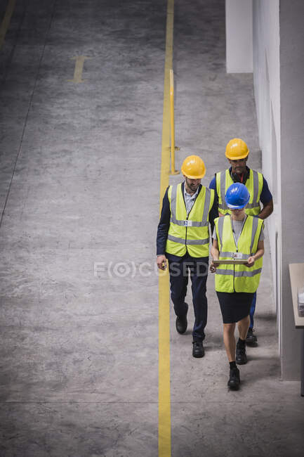 Supervisor y trabajadores con tableta digital caminando en fábrica - foto de stock