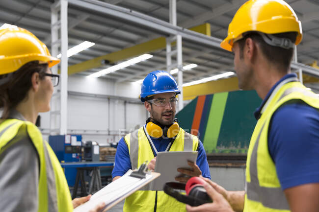 Vorgesetzter und Arbeiter mit Klemmbrett und digitalem Tablet im Gespräch in der Fabrik — Stockfoto