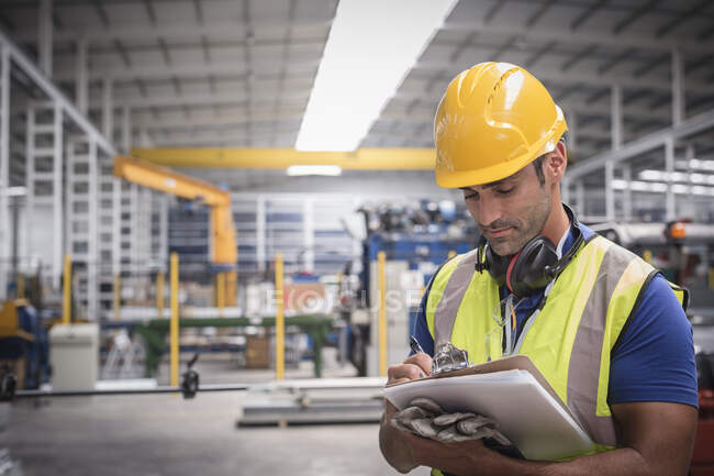 Male worker writing on clipboard in factory — Stock Photo