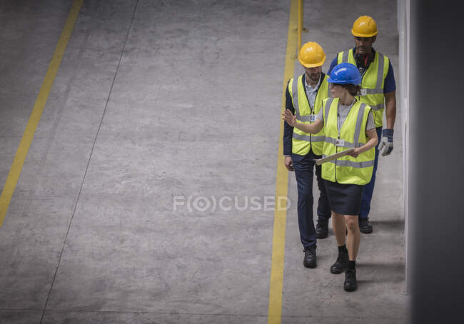 Supervisor femenino y trabajadores masculinos caminando y hablando en fábrica - foto de stock