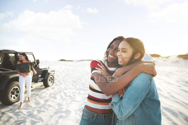 Felices jóvenes amigas abrazándose, disfrutando de un viaje por la playa - foto de stock