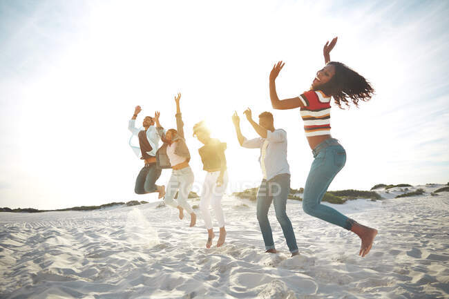 Retrato juguetón, enérgico jóvenes amigos saltando de alegría en la soleada playa de verano - foto de stock