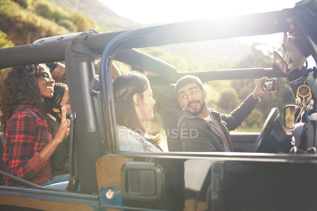 Man with digital camera taking selfie in jeep with friends — Stock Photo