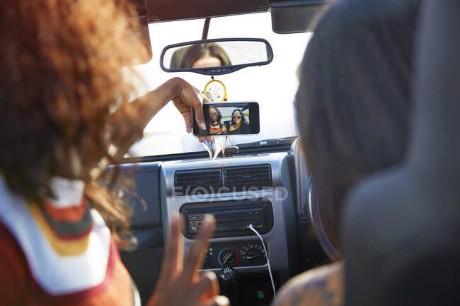 Young women friends with camera phone taking selfie, enjoying road trip in jeep — Stock Photo