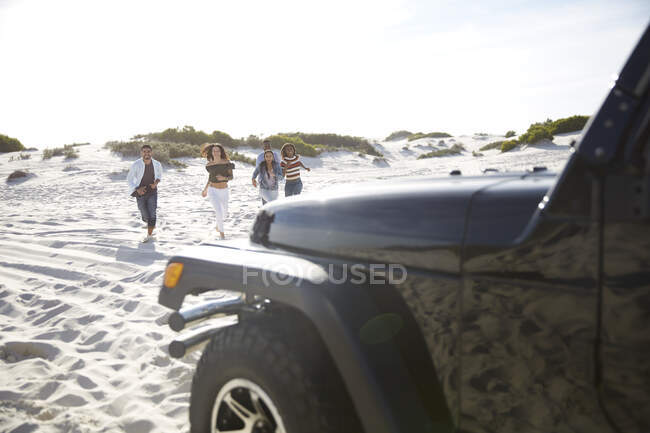 Young friends running on sunny beach toward jeep — Stock Photo