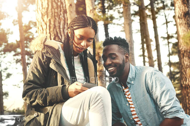 Young couple texting with smart phone in woods — Stock Photo