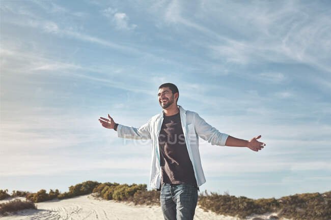 Jeune homme exubérant avec les bras tendus sur une plage ensoleillée — Photo de stock