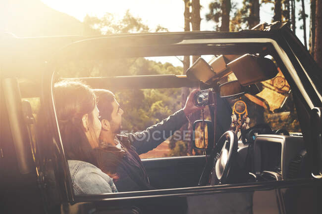 Молодая пара с цифровой планшетной камерой делает селфи в джипе в солнечных лесах — стоковое фото