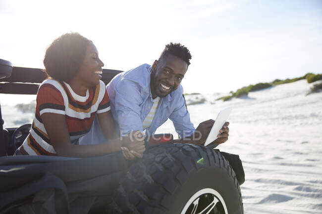 Jeune couple souriant utilisant une tablette numérique en jeep sur une plage ensoleillée — Photo de stock
