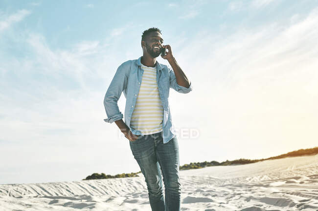 Young man talking on cell phone on sunny beach — Stock Photo