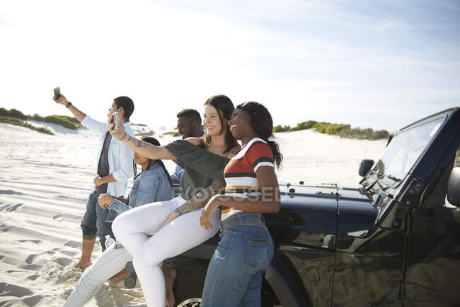 Молоді друзі з телефонами знімають селфі на джипі на сонячному пляжі — стокове фото