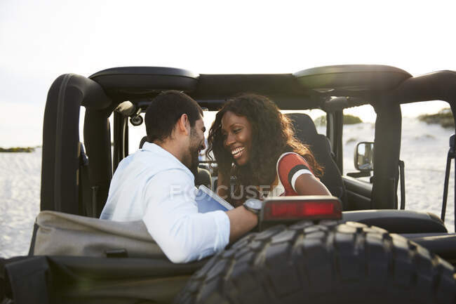 Cariñosa pareja joven sonriendo en el asiento trasero de jeep, disfrutando de viaje por carretera - foto de stock