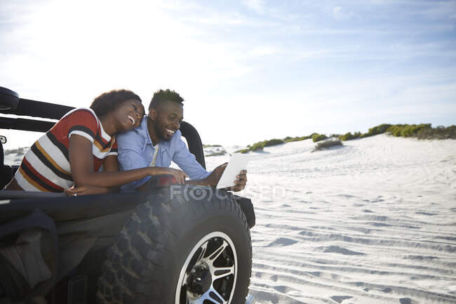 Молода пара використовує цифровий планшет у джипі на сонячному пляжі, насолоджуючись дорожньою подорожжю — стокове фото
