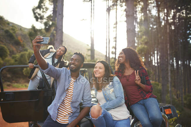 Giovani amici con fotocamera telefono scattare selfie a jeep nel bosco — Foto stock