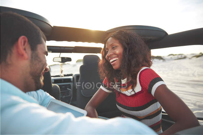 Smiling young couple riding in back seat of jeep on beach, enjoying road trip — Stock Photo