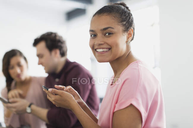 Портрет улыбается, уверенная деловая женщина смс со смартфона в офисе — стоковое фото