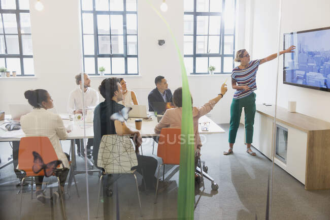 Female architect at television screen leading conference room meeting — Stock Photo