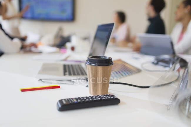 Einweg-Kaffeetasse und Fernbedienung auf dem Tisch im Konferenzraum — Stockfoto