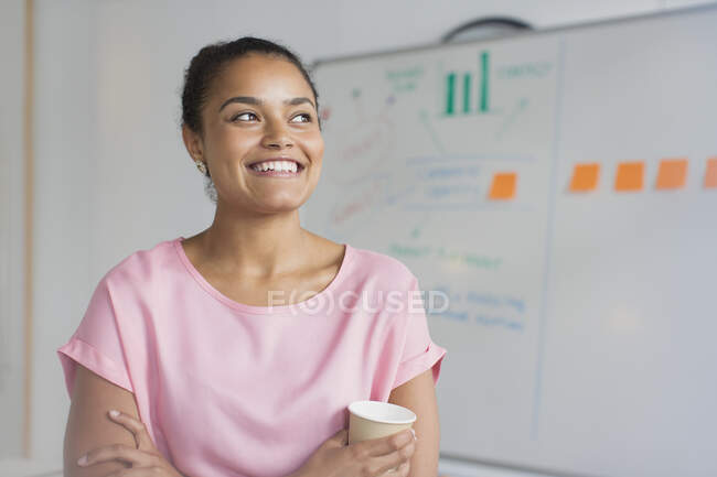 Portrait smiling, ambitious businesswoman drinking coffee at whiteboard in office — Stock Photo