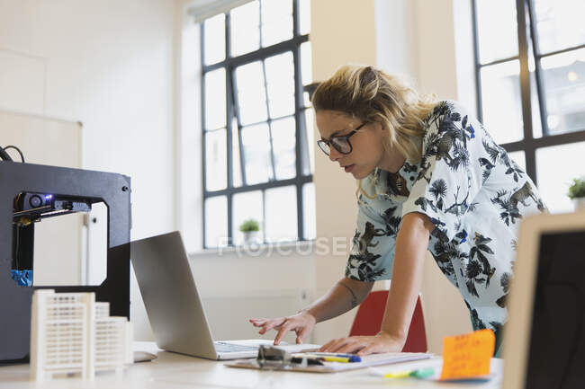 Designer feminina trabalhando no laptop ao lado da impressora 3D no escritório — Fotografia de Stock