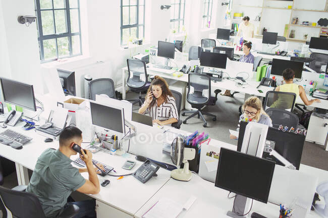 Gente de negocios trabajando en escritorios en oficinas de planta abierta - foto de stock