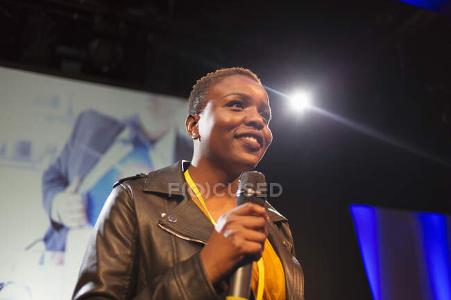 Smiling female speaker with microphone on stage — Stock Photo