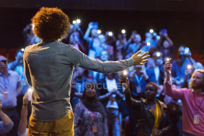 Altavoz en el escenario hablando con el público con linternas de teléfonos inteligentes - foto de stock