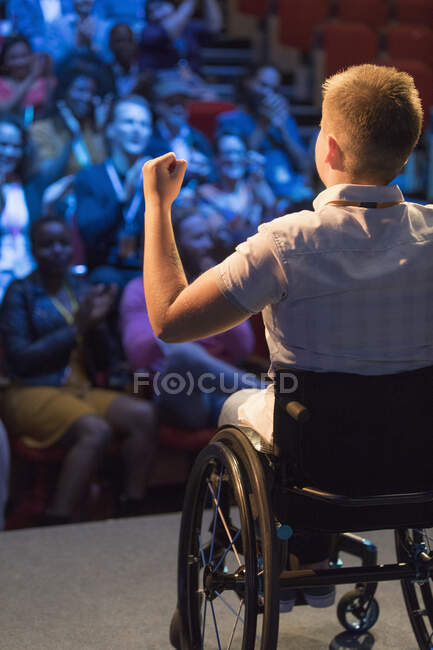 Female speaker in wheelchair gesturing on stage for cheering audience — Stock Photo