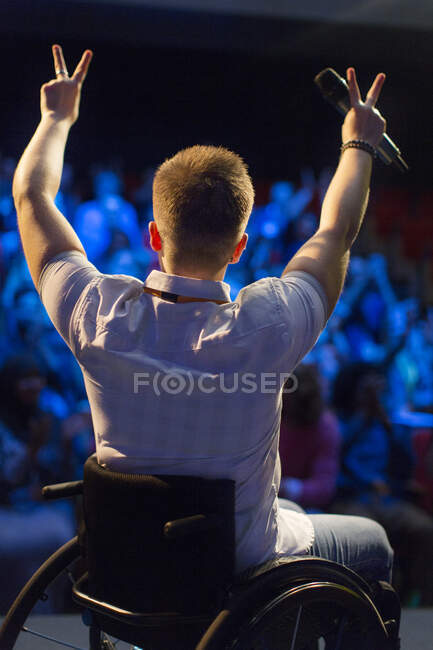 Female speaker in wheelchair gesturing peace sign on stage — Stock Photo