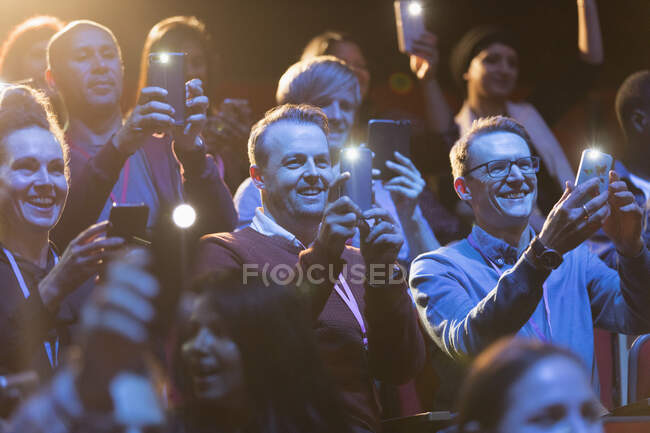 Audiencia sonriente usando linternas de teléfonos inteligentes - foto de stock