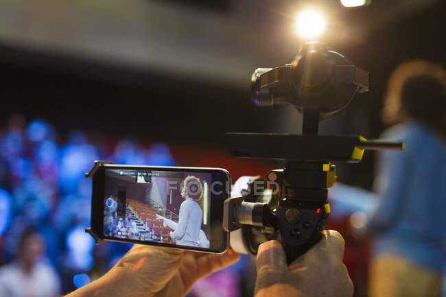 Cameraman with smart phone and equipment videoing speaker on stage — Stock Photo