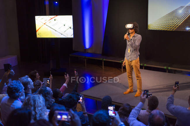 Audience watching male speaker with virtual reality simulator glasses on stage — Stock Photo