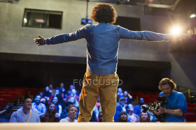 Publikum sieht männlichen Redner mit ausgestreckten Armen auf der Bühne — Stockfoto