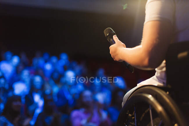 Женщина-спикер в инвалидной коляске держит микрофон на сцене — стоковое фото