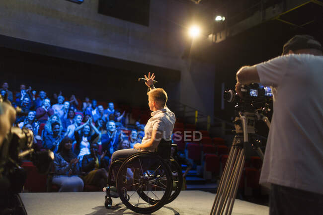 Altavoz femenino en silla de ruedas en el escenario saludando al público - foto de stock