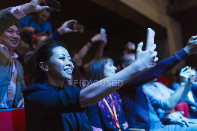 Sorrindo, mulher entusiasmada usando telefone da câmera no público escuro — Fotografia de Stock