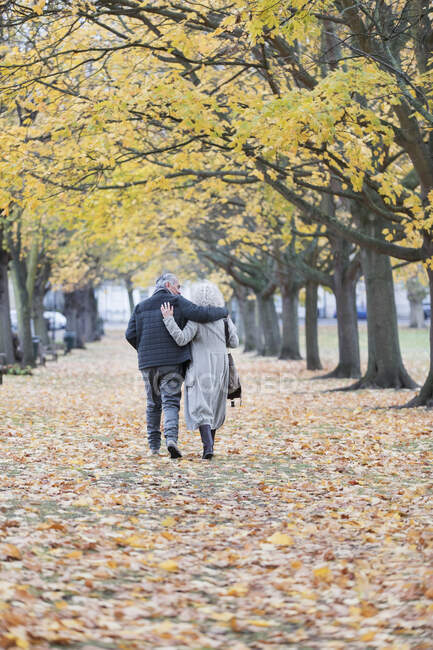 Coppia affettuosa che si abbraccia, cammina tra alberi e foglie nel parco autunnale — Foto stock