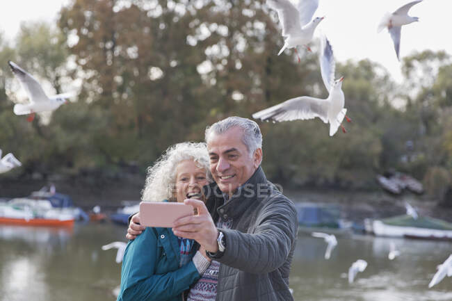 Playful senior couple taking selfie at pond in park — Stock Photo