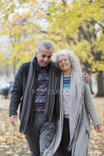 Pareja mayor segura y sonriente abrazándose y caminando en el parque de otoño - foto de stock