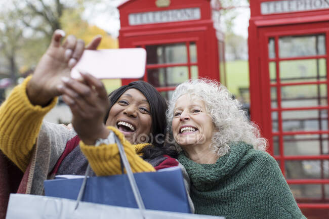 Усміхаючись старші жінки, друзі влаштовують селфі в парку перед червоними телефонними будками. — стокове фото