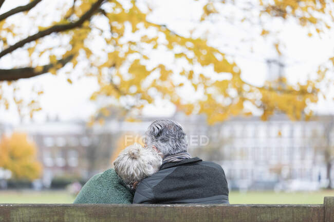 Casal sênior afetuoso abraçando no banco no parque de outono — Fotografia de Stock
