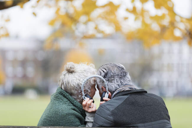 Senior couple sharing headphones, listening to music in autumn park — Stock Photo