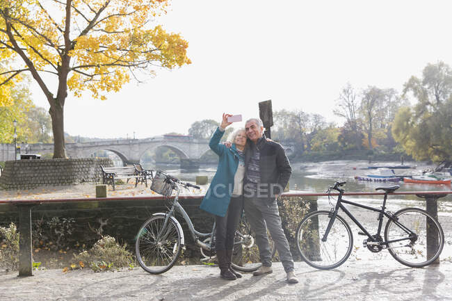 Coppia senior con biciclette scattare selfie al fiume autunno — Foto stock