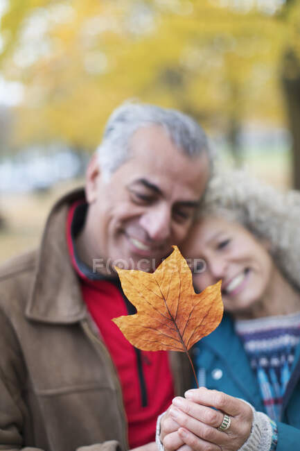 Cariñosa pareja de ancianos sosteniendo hoja de otoño naranja - foto de stock