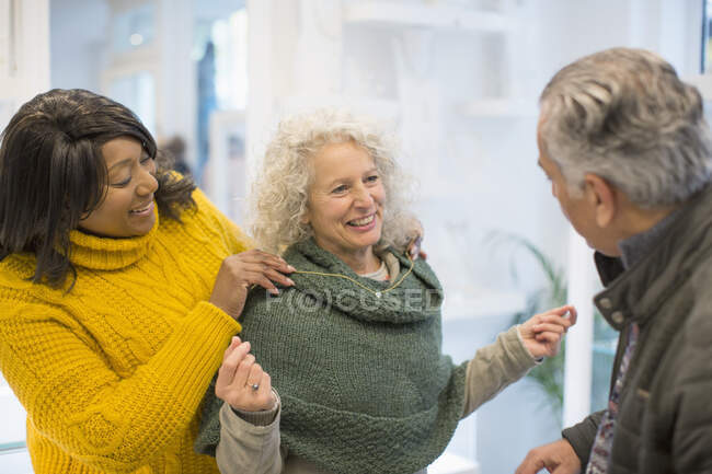 Asistente de ventas ayudando a la mujer mayor a probar joyas en la tienda - foto de stock