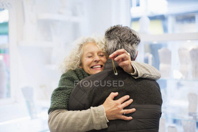 Усміхнена старша жінка обіймає чоловіка в магазині ювелірних виробів — стокове фото