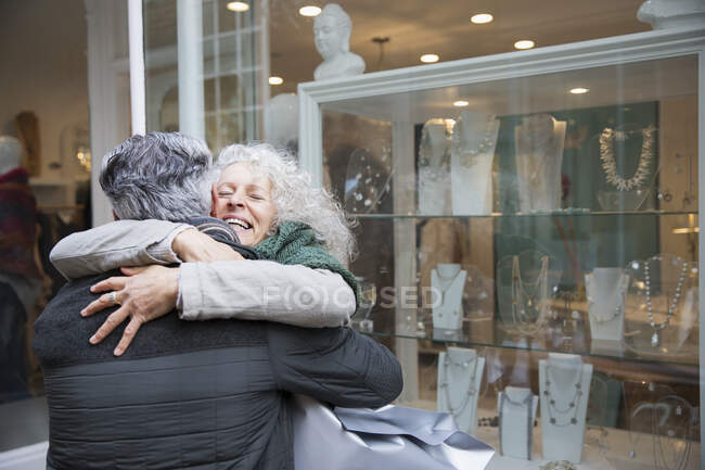 Senior couple hugging, window shopping at jewelry storefront — Stock Photo