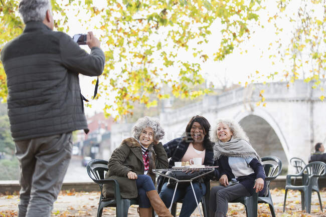 Senior man photographing active senior women friends at autumn park cafe — Stock Photo