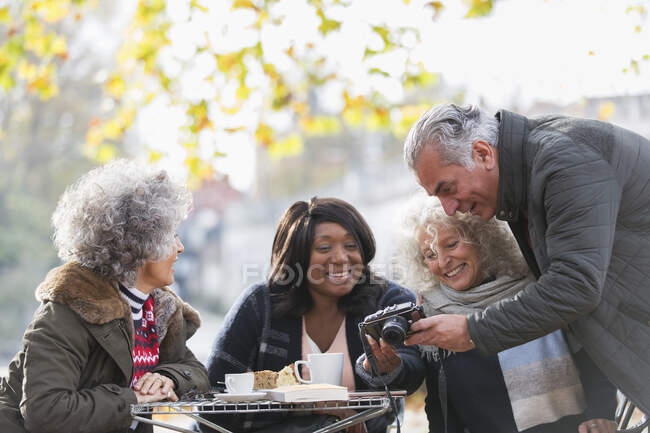 Active senior friends using digital camera at autumn sidewalk cafe — Stock Photo
