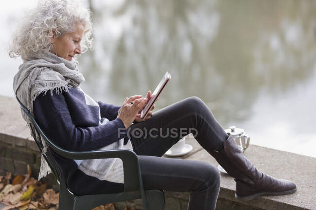 Активна старша жінка, використовуючи цифровий планшет у парковому ставку — стокове фото